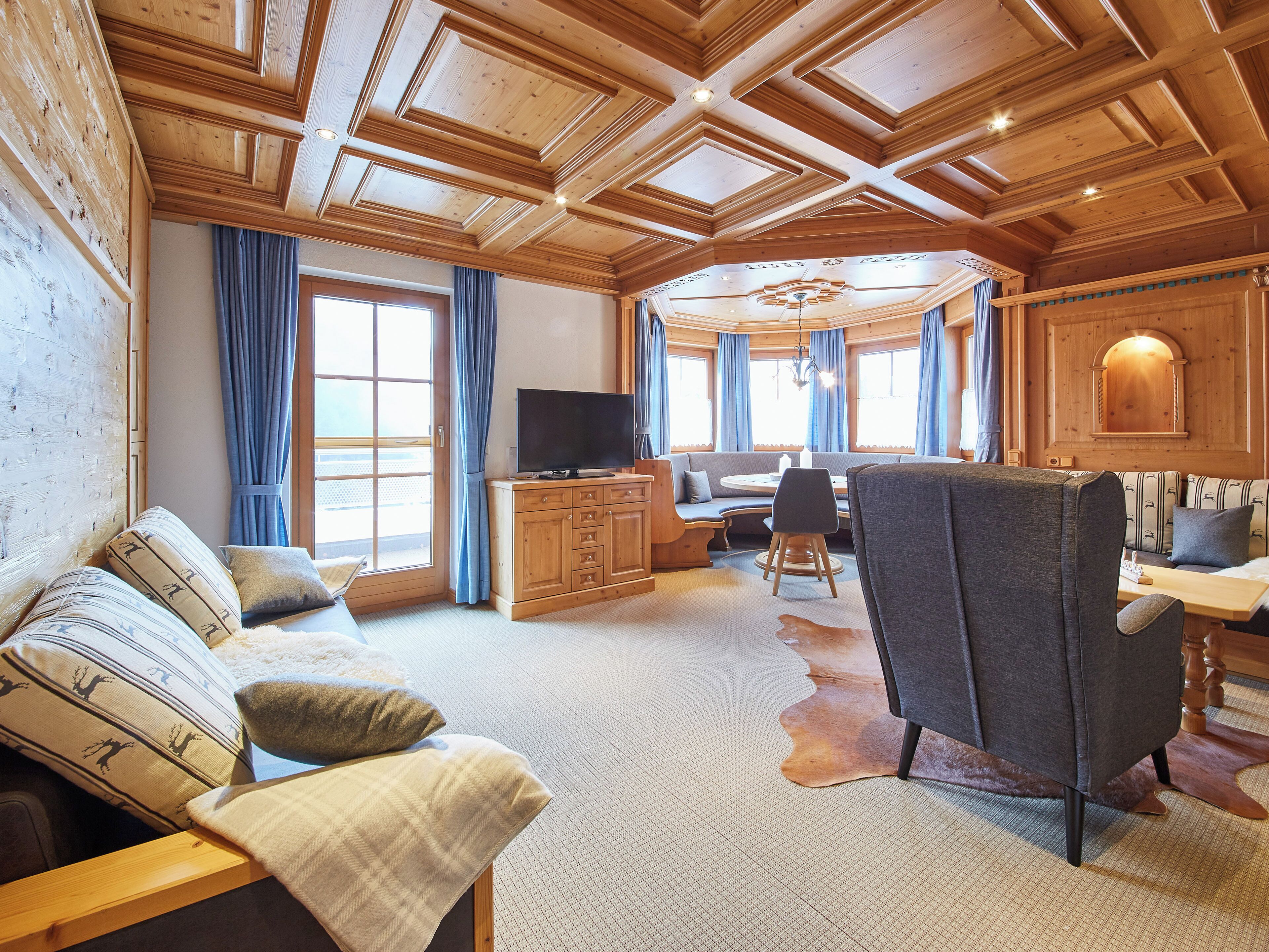 A cozy cabin interior with a wooden ceiling, a sofa, a dining table, and a TV.