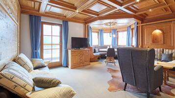 A cozy cabin interior with a wooden ceiling, a sofa, a dining table, and a TV.