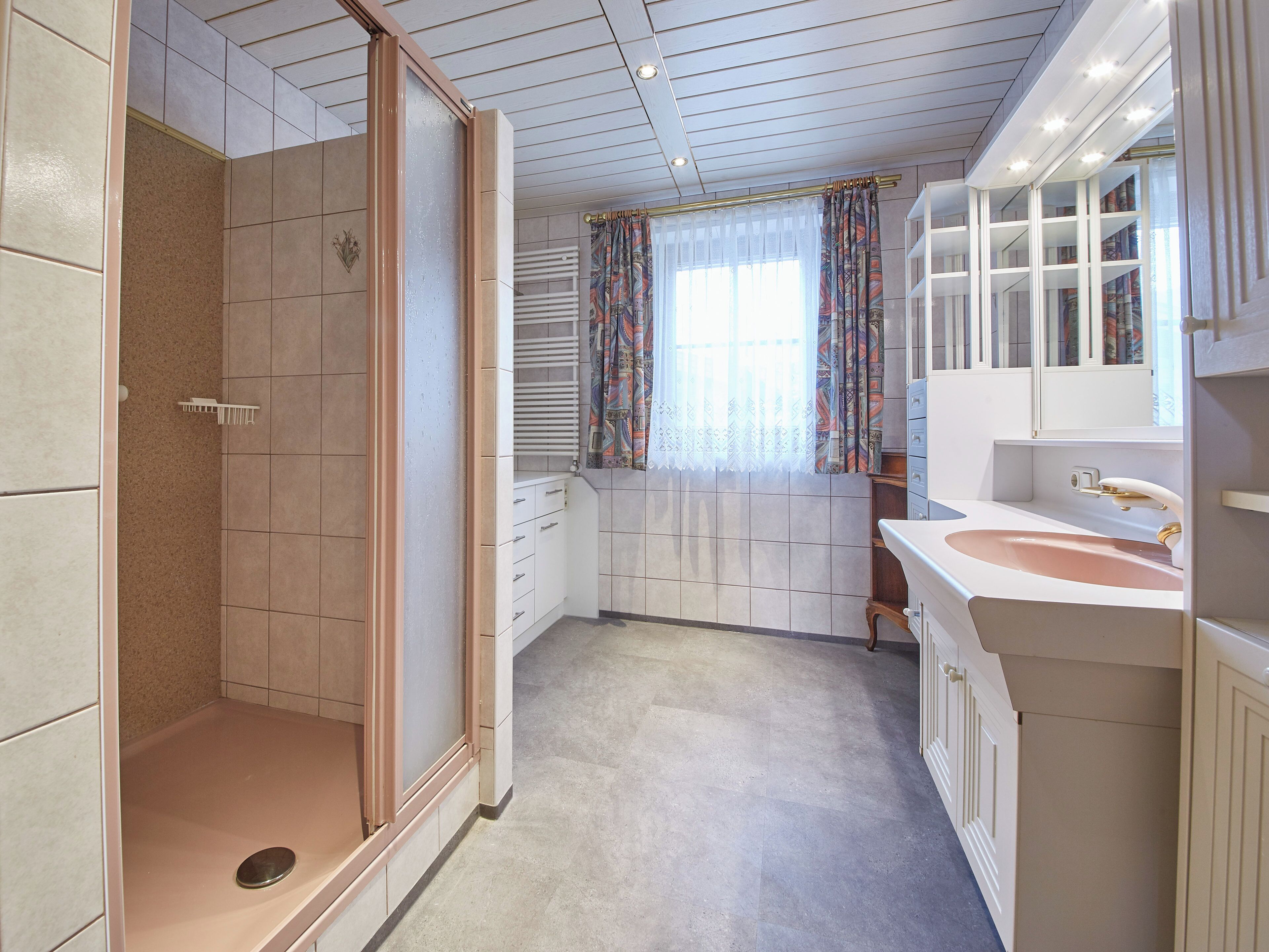 A bathroom with a shower, a sink, and a window with curtains.