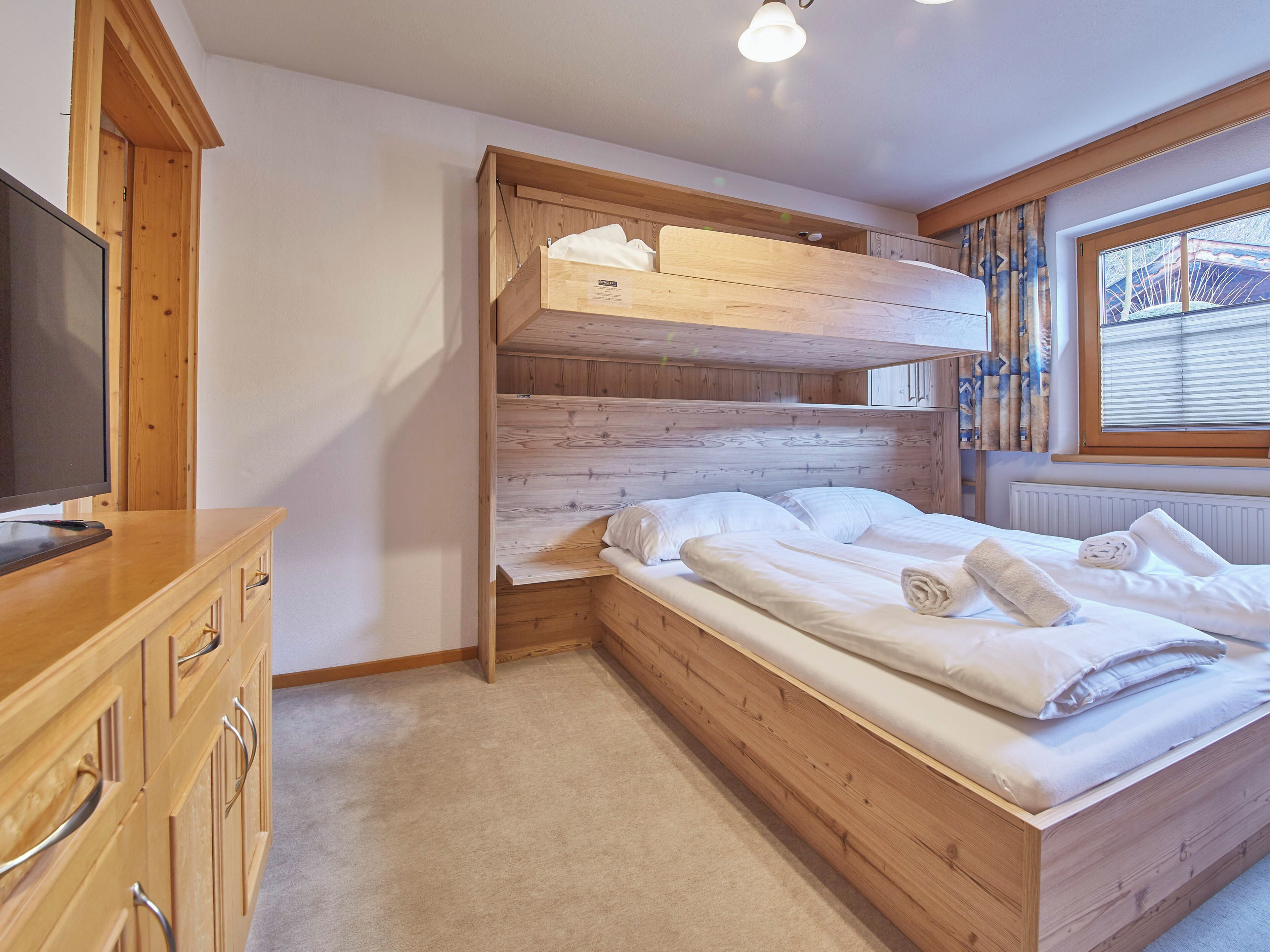 A bunk bed with a wooden headboard, a TV on a wooden cabinet, and a window with curtains.