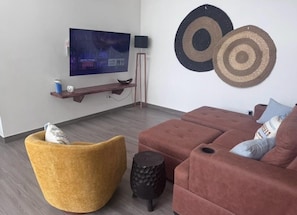 A modern living room with a flat-screen TV, a brown sofa, a yellow chair, and two wall-mounted circular rugs. - Casa Aurora Oasis with Private Patio & Pool (Playas Del Coco)
