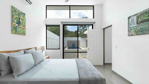 A modern bedroom with a large bed, a sliding glass door to a balcony, and two paintings on the walls. - Casa Aurora with Private Patio & Pool (Playas Del Coco)