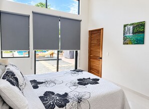 A bedroom with a bed, a window with blinds, a door, and a painting on the wall.