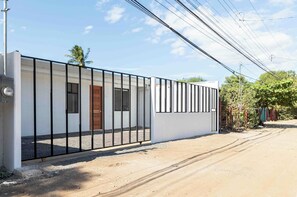 A modern building with a white exterior, a black metal fence, and a wooden door. - Casa Aurora Oasis with Private Patio & Pool (Playas Del Coco)