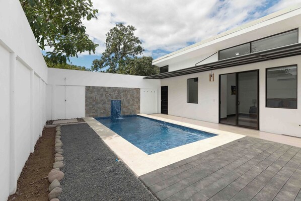 A modern house with a swimming pool, a stone wall, and a covered patio area. - Casa Aurora with Private Patio & Pool (Playas Del Coco)