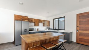 A modern kitchen with wooden cabinets, a stainless steel refrigerator, a large island with bar stools, and a window above the sink. - Casa Aurora with Private Patio & Pool (Playas Del Coco)
