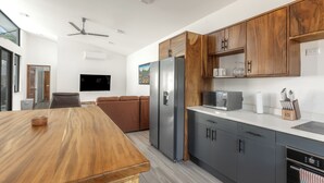 A modern kitchen with wooden cabinets, a stainless steel refrigerator, a microwave, and a dining area with a wooden table. - Casa Aurora with Private Patio & Pool (Playas Del Coco)