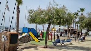 A sunny outdoor area with a playground, benches, and palm trees.