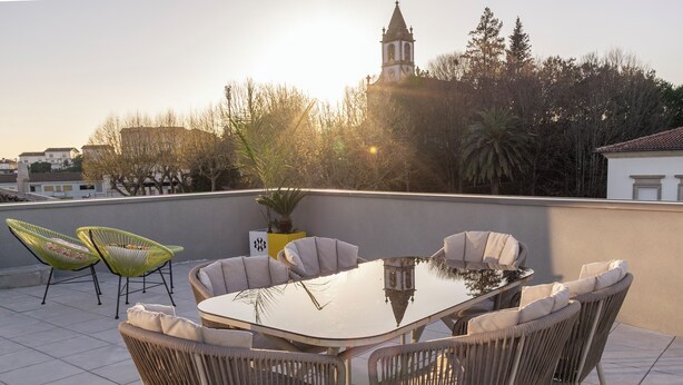 Eine Dachterrasse mit einem runden Tisch und Korbstühlen, mit Blick auf eine Stadtlandschaft und einen Kirchturm.