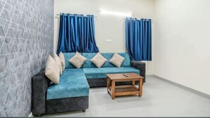 A living room with a sectional sofa, a wooden coffee table, and blue curtains. - 2-bedroom apartment in enjoyable Hyderabad with WiFi, AC (Hyderabad)
