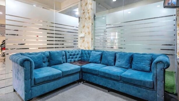 A modern room with a blue sectional sofa, a glass partition wall, and a ceiling with recessed lighting. - 2-bedroom apartment in enjoyable Hyderabad with WiFi, AC (Hyderabad)