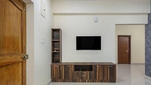 A room with a wooden door, a built-in entertainment unit with a TV, and a tiled floor. - 2-bedroom apartment in enjoyable Hyderabad with WiFi, AC (Hyderabad)