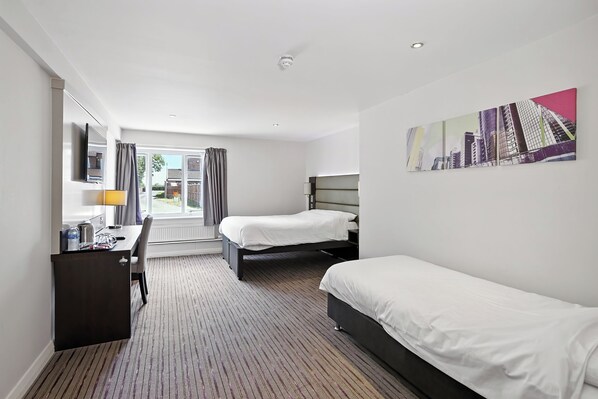 Une chambre d’hôtel avec deux lits simples, un bureau avec une chaise, un téléviseur à écran plat et une grande fenêtre avec des rideaux.
