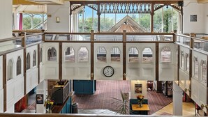 Un intérieur spacieux avec un plafond haut, des rampes en bois et de grandes fenêtres offrant une vue sur l’extérieur.