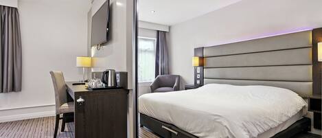 Habitación de hotel con una cama grande, un escritorio con silla, un televisor montado en la pared y una ventana con cortinas.
