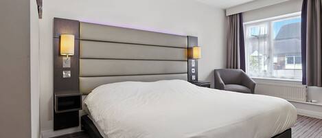 Una habitación de hotel moderna con una cama grande, dos lámparas fijadas a la pared, una silla y una ventana con cortinas.