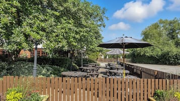 An outdoor patio area with wooden tables and benches, surrounded by a wooden fence and lush greenery.