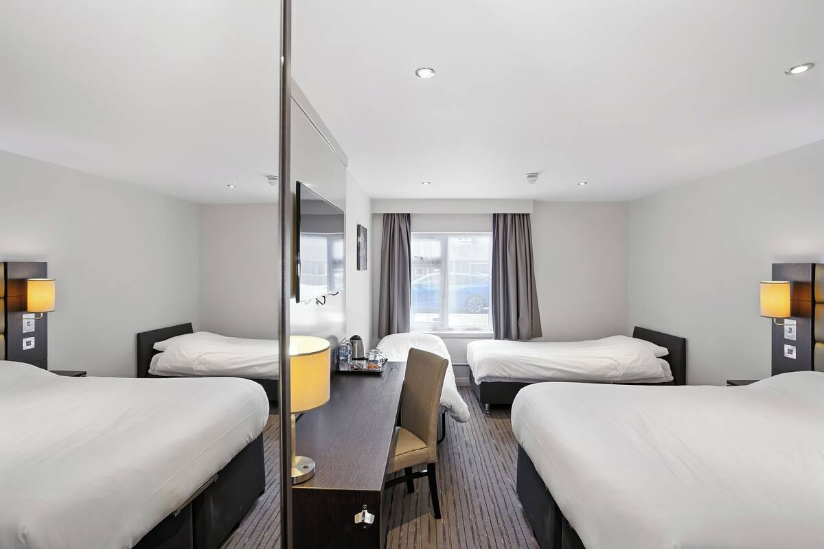 Ein Hotelzimmer mit zwei Einzelbetten, einem Schreibtisch mit Stuhl, einem großen Spiegel und einem Fenster mit Vorhängen.