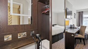 A hotel room with a wooden panel wall, a bed, a desk with a chair, a mirror, and a bathroom with a towel rack.