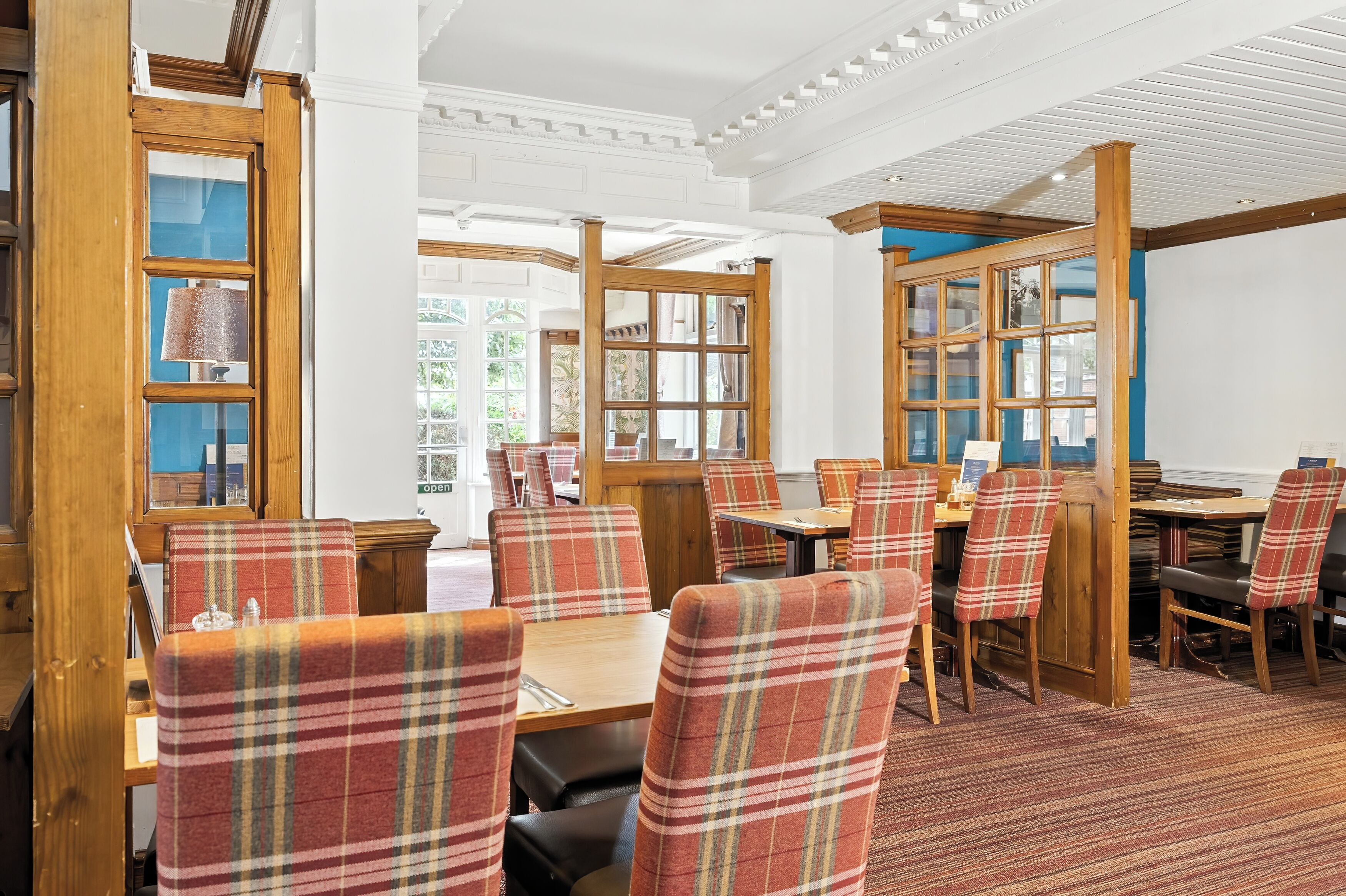 A restaurant with wooden tables and chairs, large windows, and a patterned carpet.