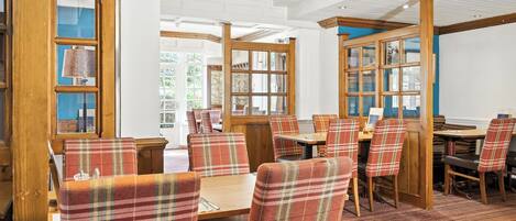 A restaurant with wooden tables and chairs, large windows, and a patterned carpet.