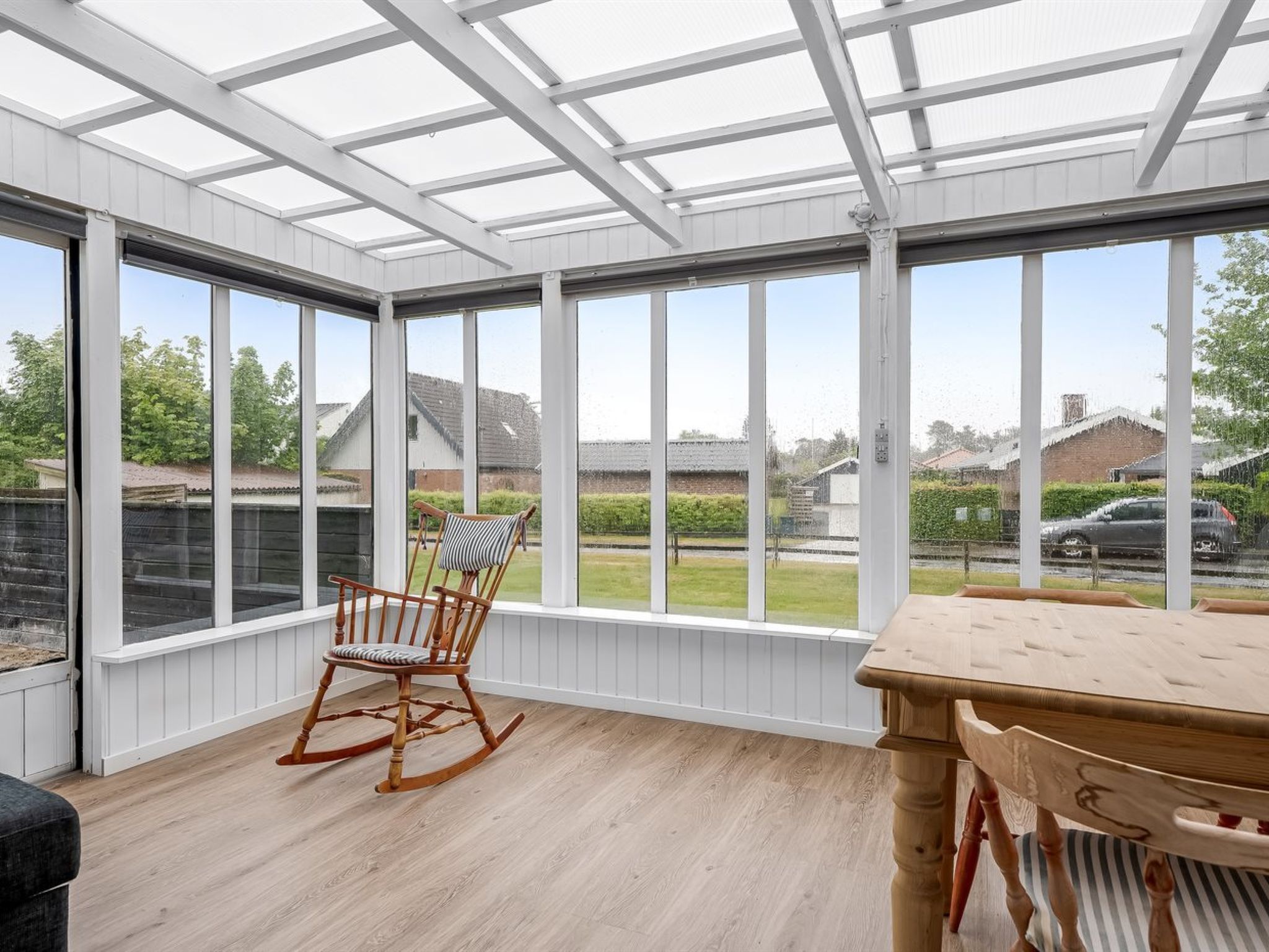 A conservatory with large windows, a rocking chair, and a wooden table.