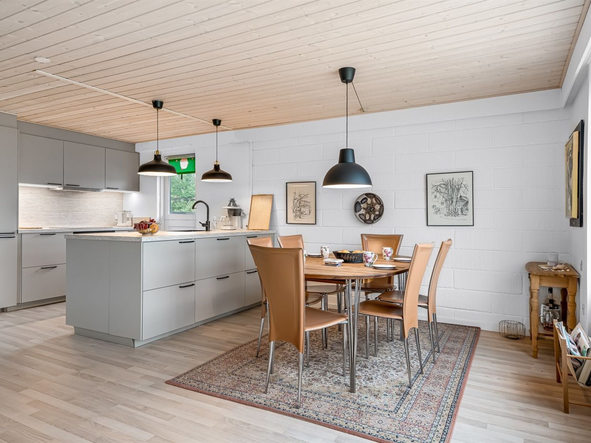 A modern kitchen with a central island, pendant lighting, and a dining area with chairs and a table.