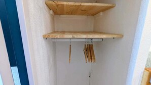 A corner of a room with a wooden shelf unit against the wall, a hanging rack with wooden items, and a visible electrical outlet. - Cozy studio for 4 in Châtel with terrace and parking (Châtel)