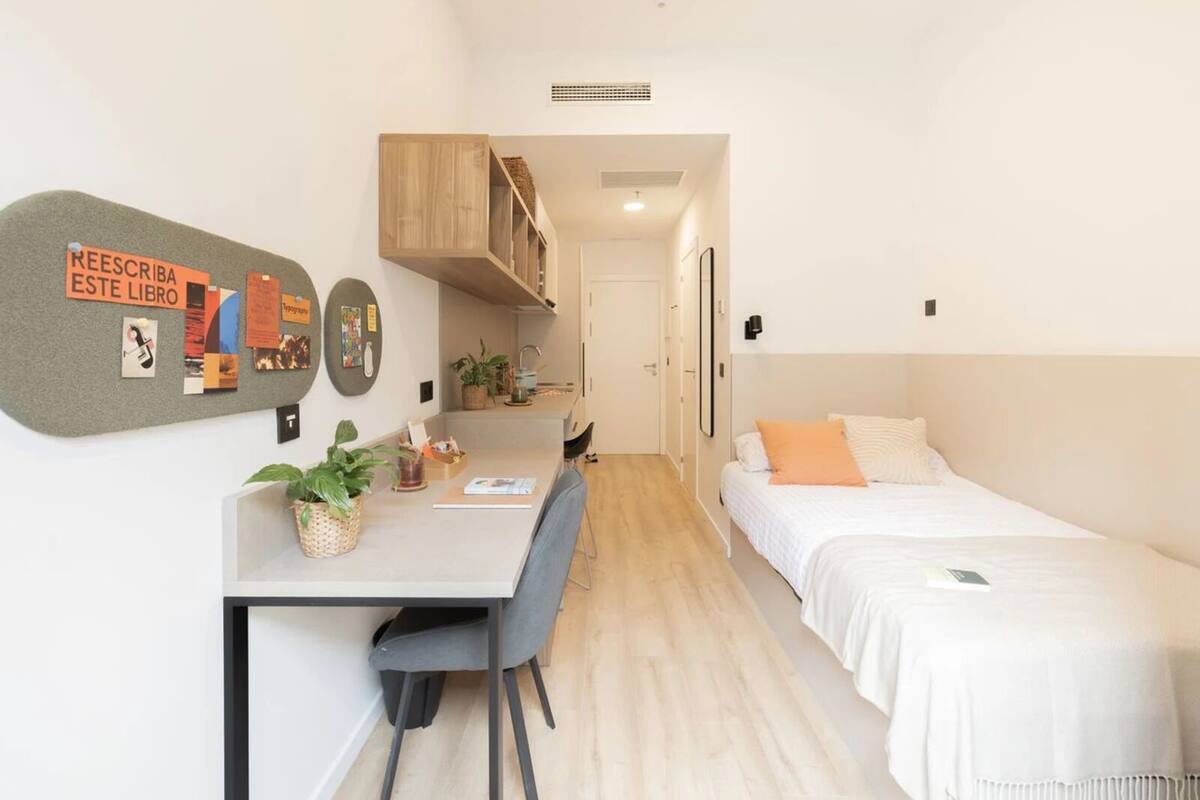 Une chambre d’hôtel compacte comprenant un coin cuisine, un petit espace repas et un lit simple.