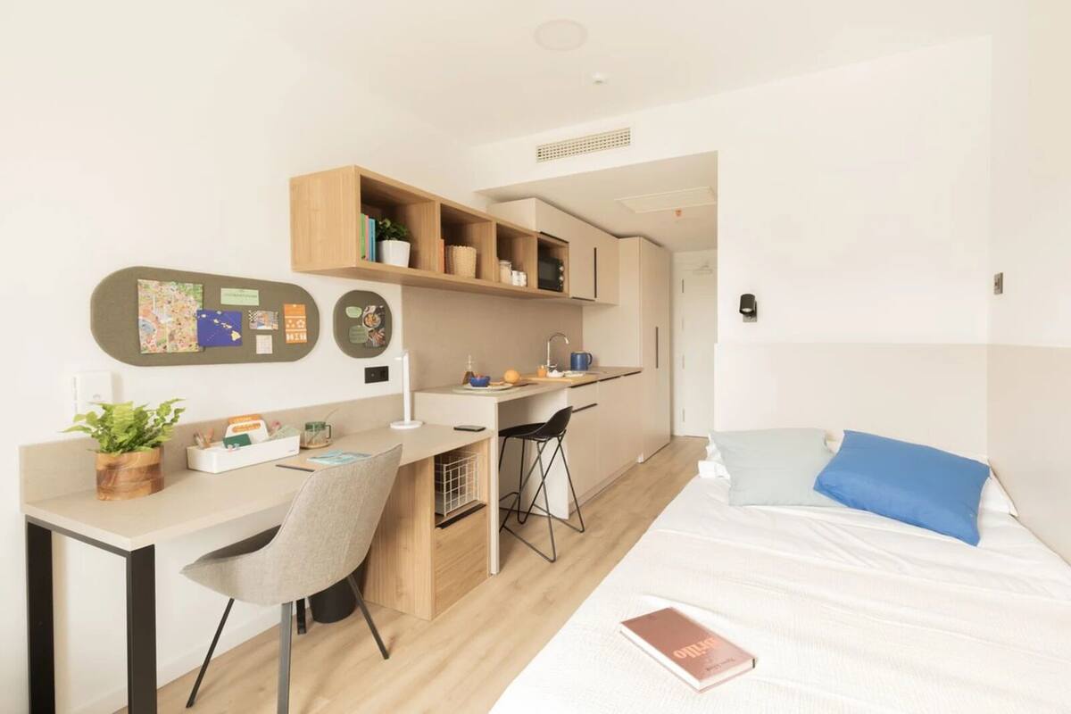 Une chambre d’hôtel de taille réduite, comprenant un lit, un bureau et une kitchenette.