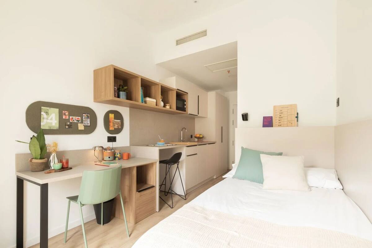 Une chambre compacte et moderne, équipée d’un lit, d’un bureau et d’une kitchenette.