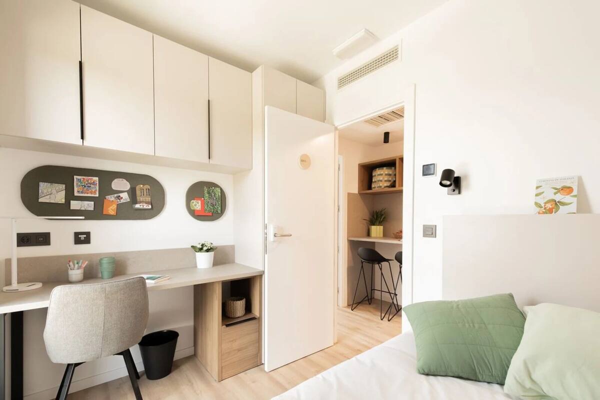 Une chambre moderne avec un lit, un bureau et une chaise. Une porte donne accès à une salle de bain.