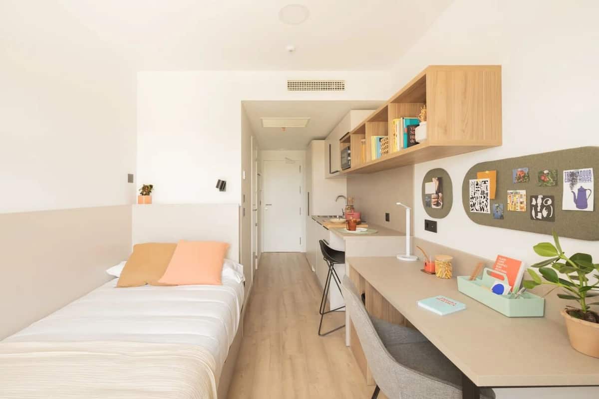 Une chambre moderne et bien éclairée, équipée d’un lit, d’un bureau et d’une kitchenette.