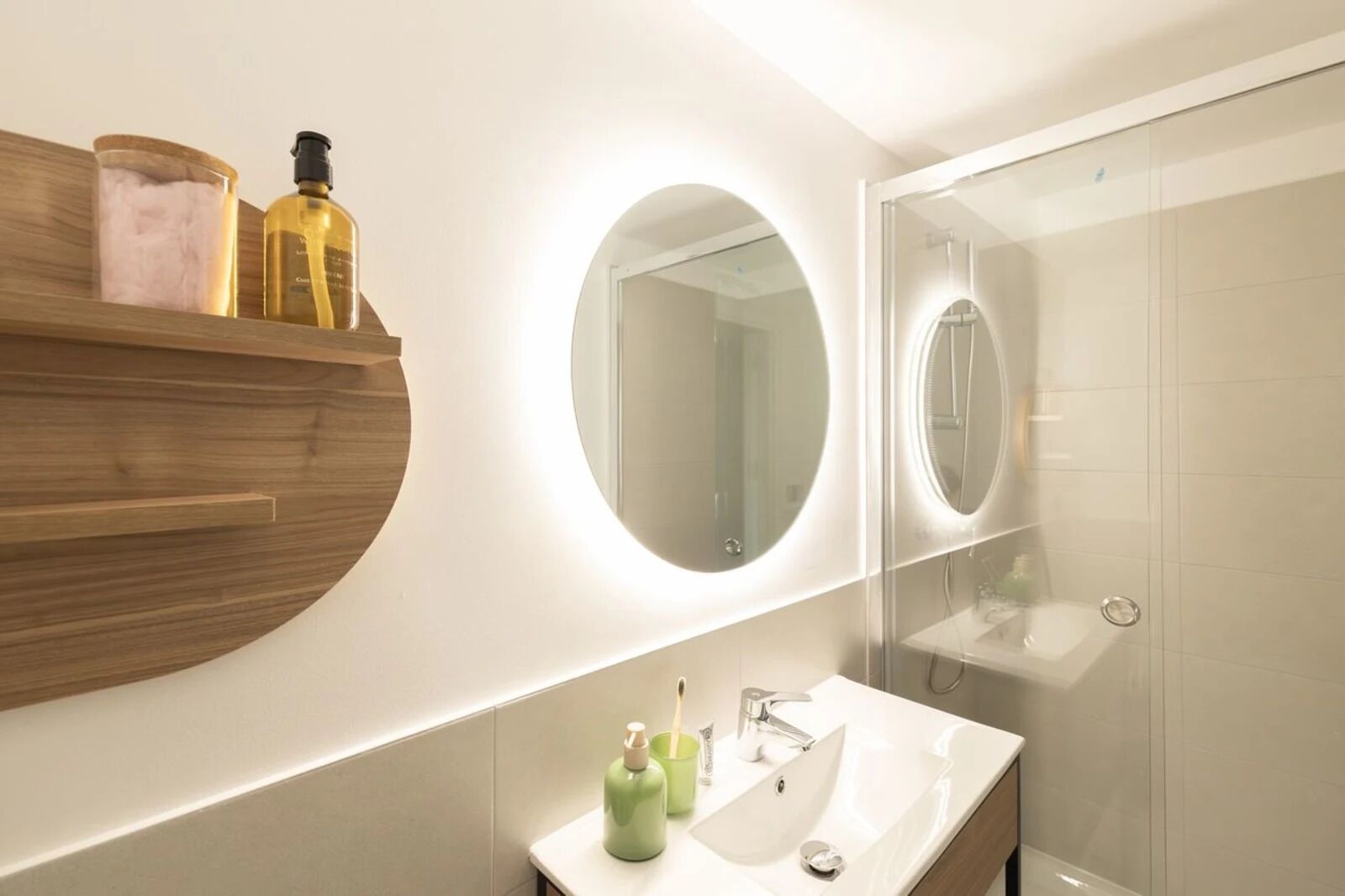 Une salle de bain moderne avec un meuble-lavabo en bois, un miroir rond et une cabine de douche en verre.