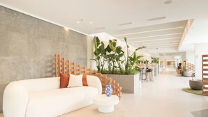 Eine moderne Hotellobby mit einem weißen Sofa, einem Couchtisch und einem großen Pflanzgefäß mit tropischen Pflanzen.