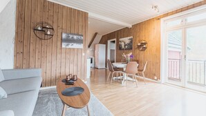 A modern living room with a wooden wall, a grey sofa, a wooden coffee table, and a dining area with chairs and a table. - Top-Floor Apartment – 5 Min Walk to Lillehammer’s Main Street (Innlandet)