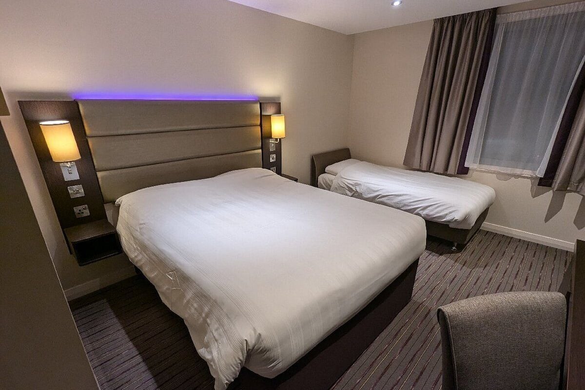 Ein Hotelzimmer mit zwei Betten, einem Sessel und einem Fenster mit Vorhängen.