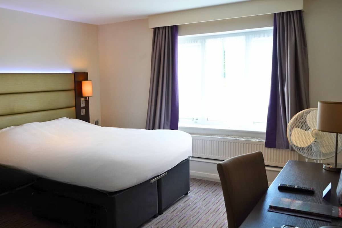 Ein Hotelzimmer mit einem großen Bett, Nachttischlampen, einem Schreibtisch mit Stuhl und einem Fenster mit Vorhängen.