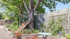 Eine Terrasse mit Holztisch und -stühlen, umgeben von erhöhten Pflanzkästen mit verschiedenen Pflanzen.
