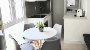Cocina compacta con armarios blancos, encimera negra y un lavamanos. Hay una mesa de comedor con cuatro sillas y una planta en maceta.