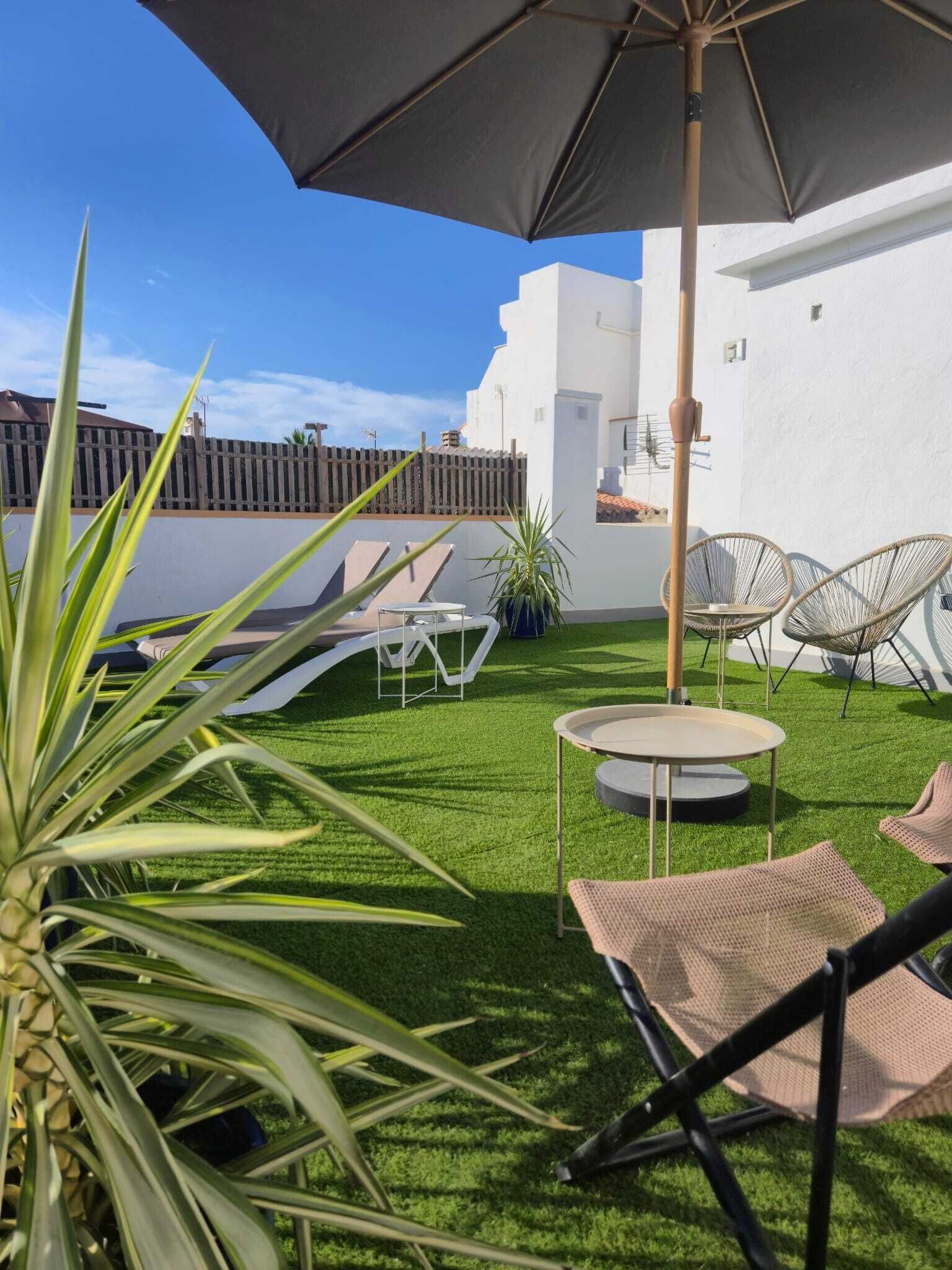 A patio with artificial grass, a round table, two wicker chairs, and a large umbrella.