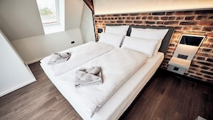 Quarto moderno com parede de tijolos, uma cama grande com roupa de cama branca e uma mesa de cabeceira com abajur.