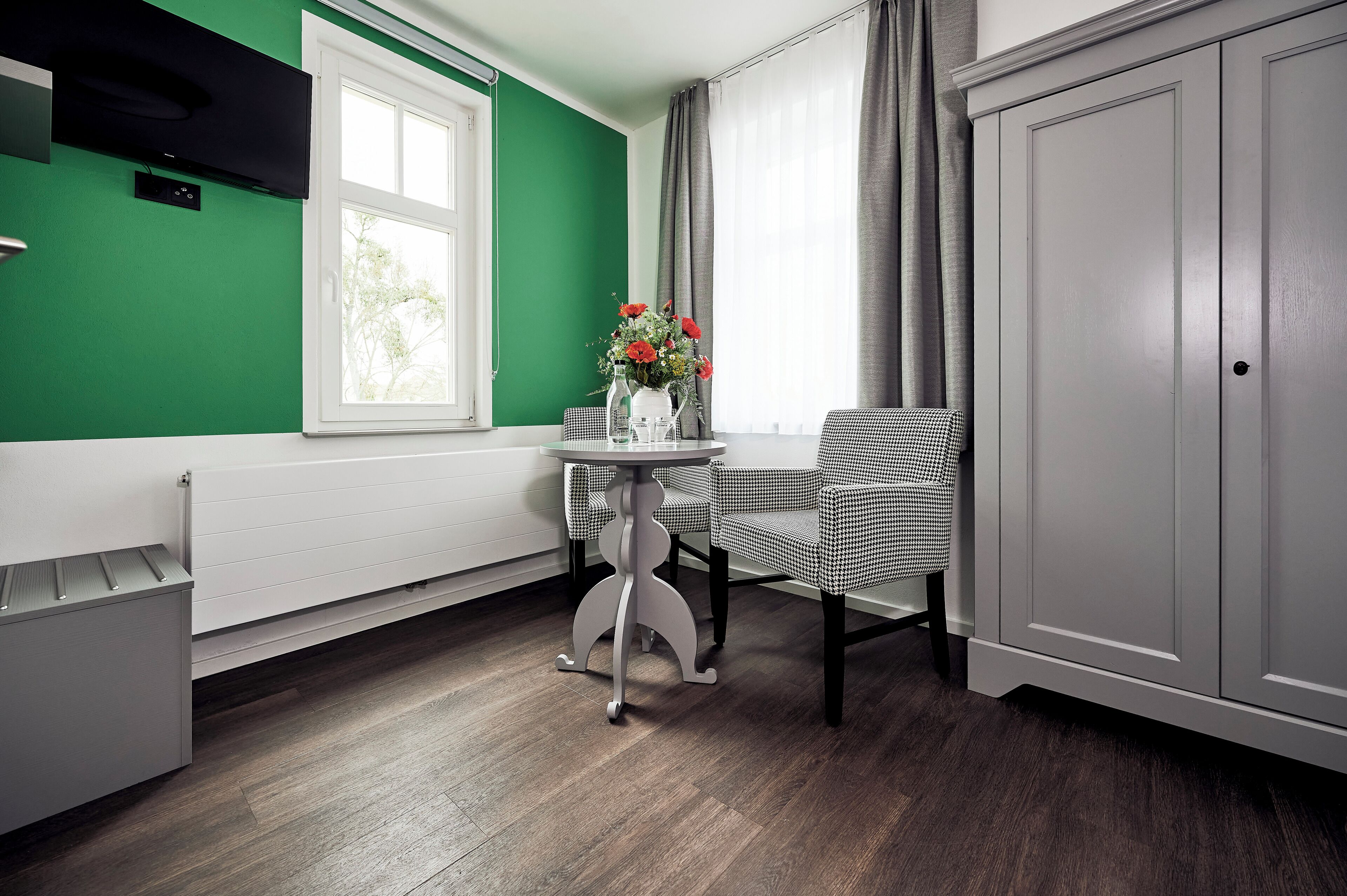 A modern kitchen with a green wall, a white radiator, a table with chairs, and a cabinet.