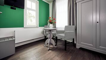 A modern kitchen with a green wall, a white radiator, a table with chairs, and a cabinet.