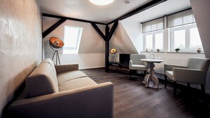 Um quarto moderno em estilo loft, com teto inclinado, um sofá acolhedor, uma mesa de jantar com cadeiras e uma grande janela com persianas decorativas.