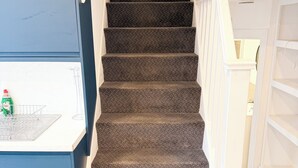 Eine Treppe mit Teppichstufen, eine weiße Wand mit einem Bild und eine blaue Wand mit einem weißen Regal.