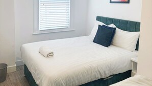 Ein Schlafzimmer mit Bett, Fenster mit Jalousien, einem Wandbild und einer Deckenleuchte.