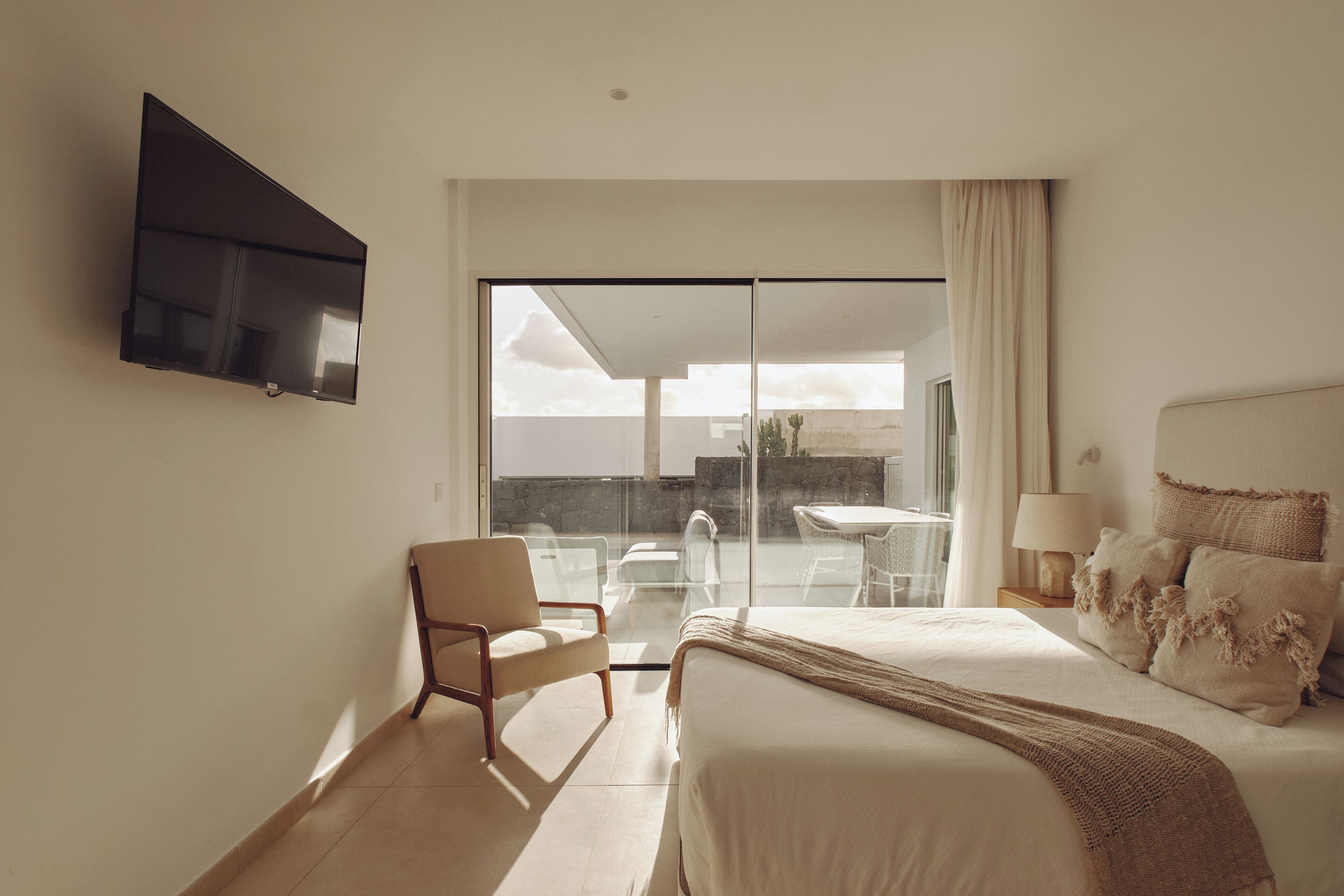 A hotel room with a bed, a chair, a television, and a view of the outdoors.