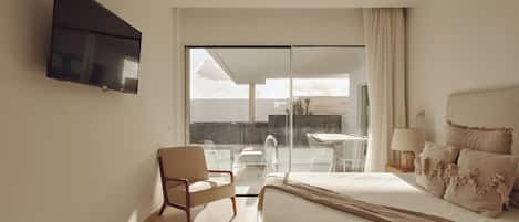 A hotel room with a bed, a chair, a television, and a view of the outdoors.
