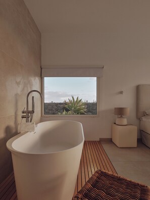Une salle de bain moderne avec une baignoire sur pieds, une fenêtre donnant sur un paysage rocheux et une table de chevet avec une lampe.